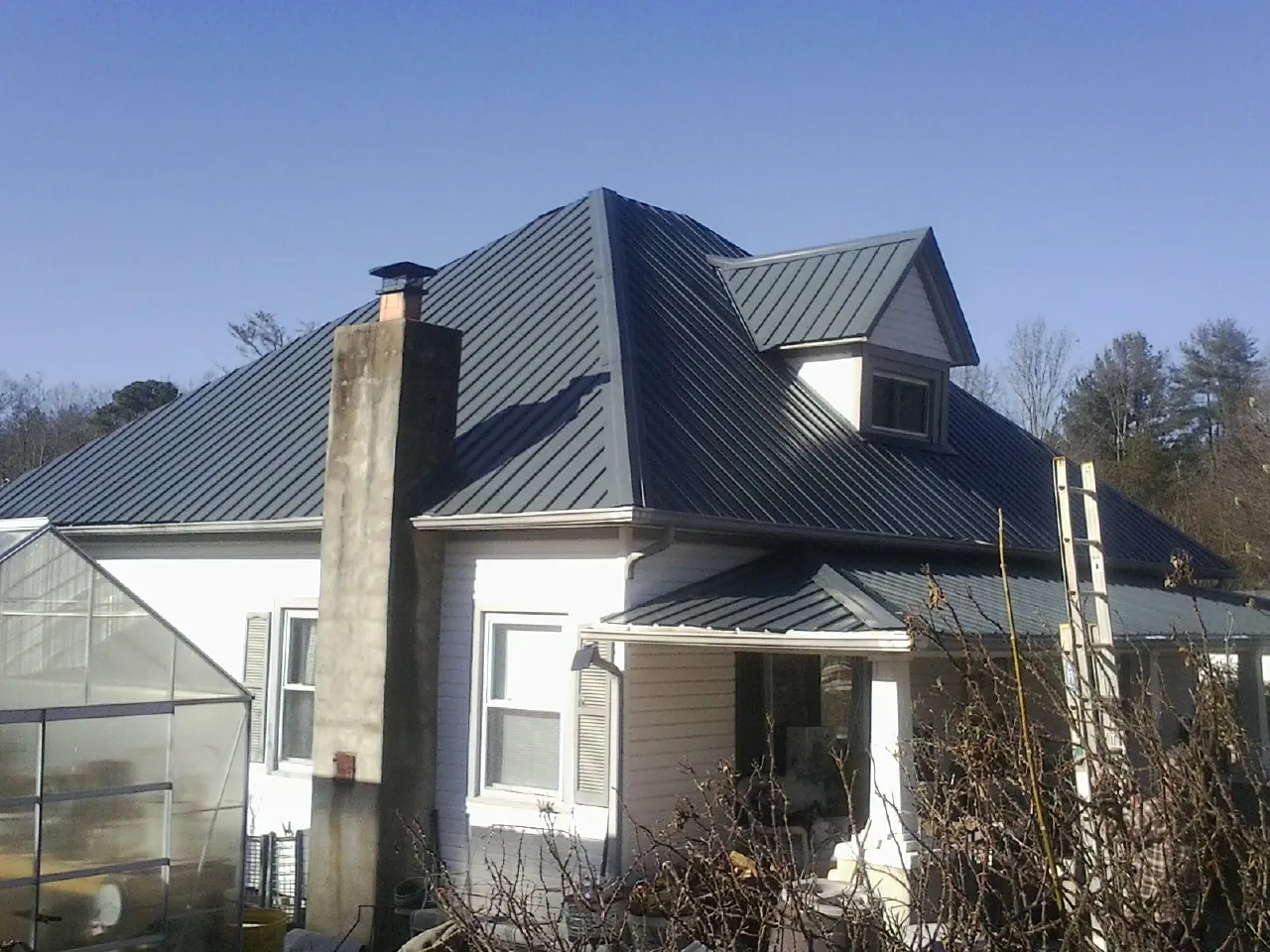 Dark blue standing seam metal roof on a white farmhouse with dormer — Slate & Tile Roof Repair by Roofing Brothers in Dell Rapids