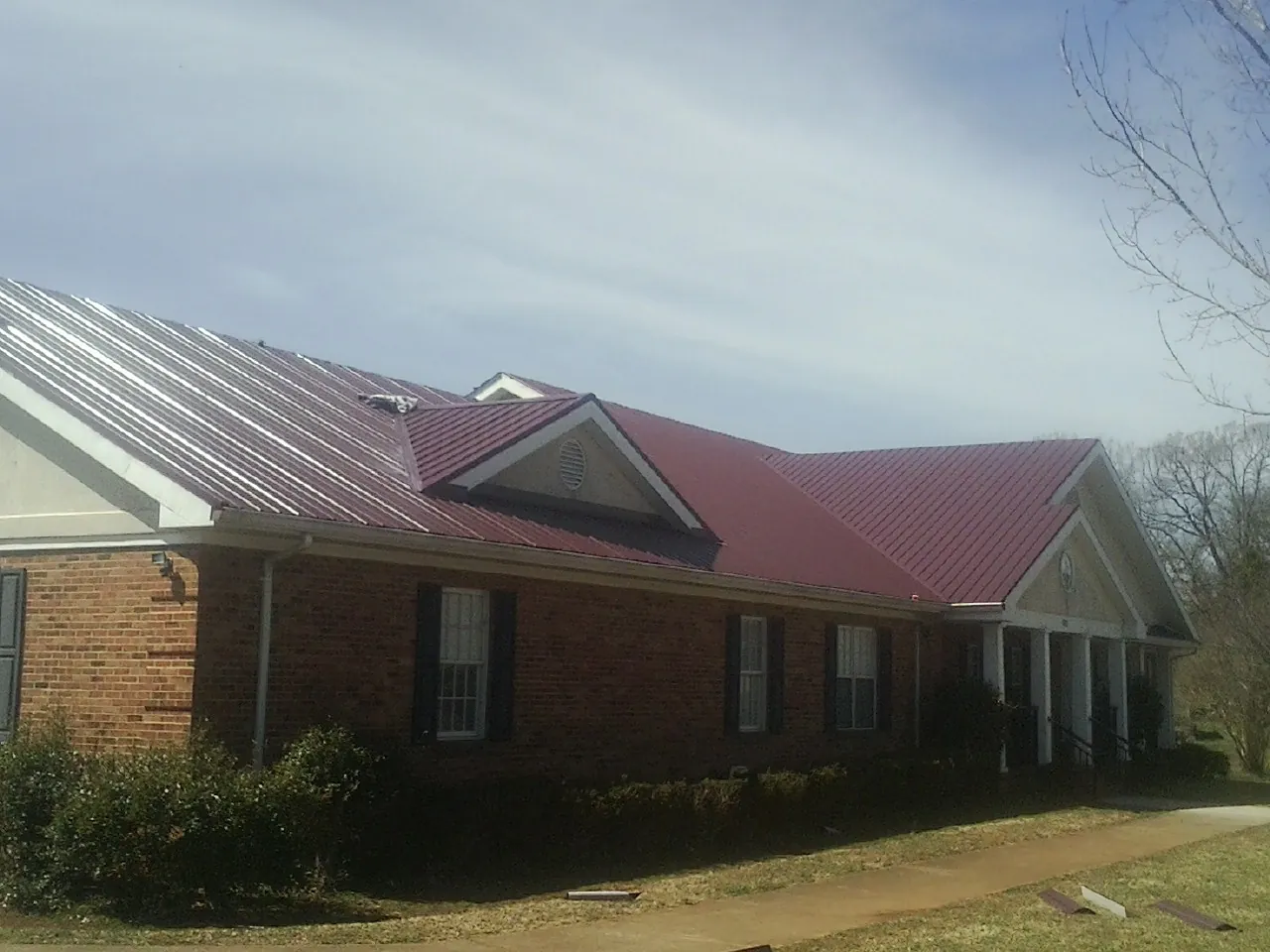 Red metal roof with gabled entries on a long brick building, from a Hail Damage Roof Repair job in Dell Rapids