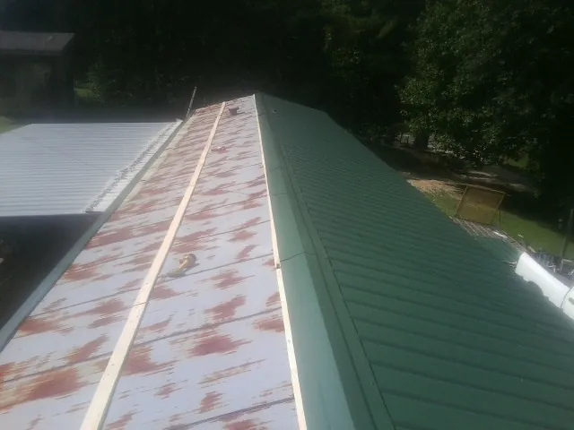 Old rusted panels beside newly installed green metal roofing — Wind Damage Roof Repair by Roofing Brothers in Dell Rapids