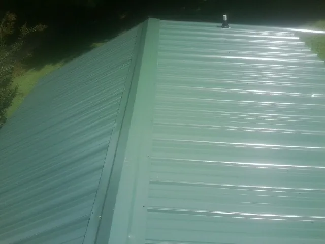 New green metal panels meeting at the ridge of a roof — Flat Roof Repair work by our crew in Dell Rapids