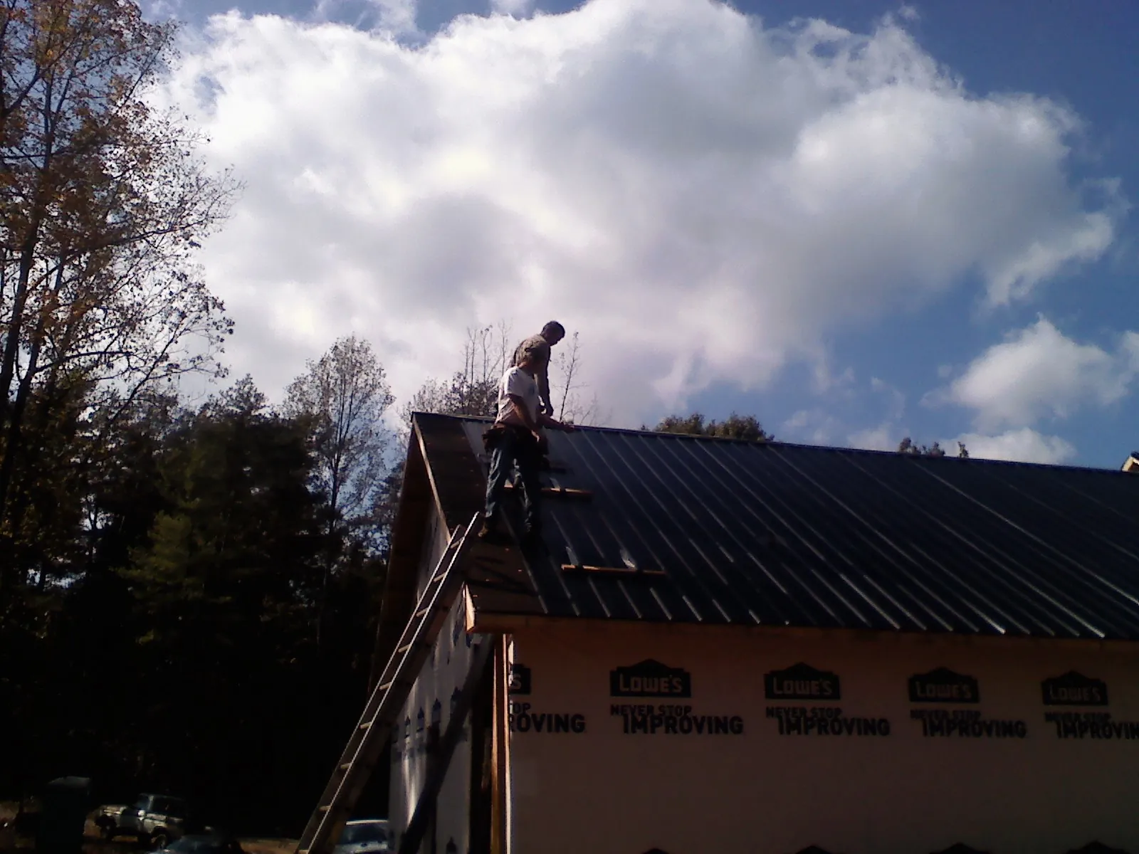 Roofer fastening dark metal panels high against a cloudy sky, from a Roof Inspection job in Dell Rapids