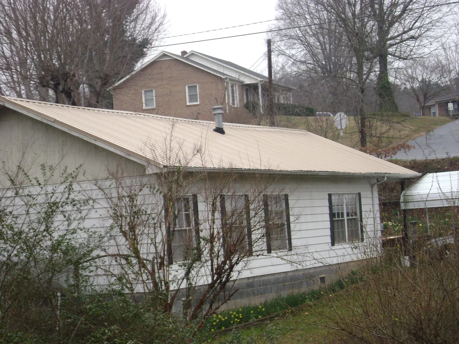 Tan metal roof on a white sided house set into a hillside — Commercial Roofing by Roofing Brothers in Dell Rapids