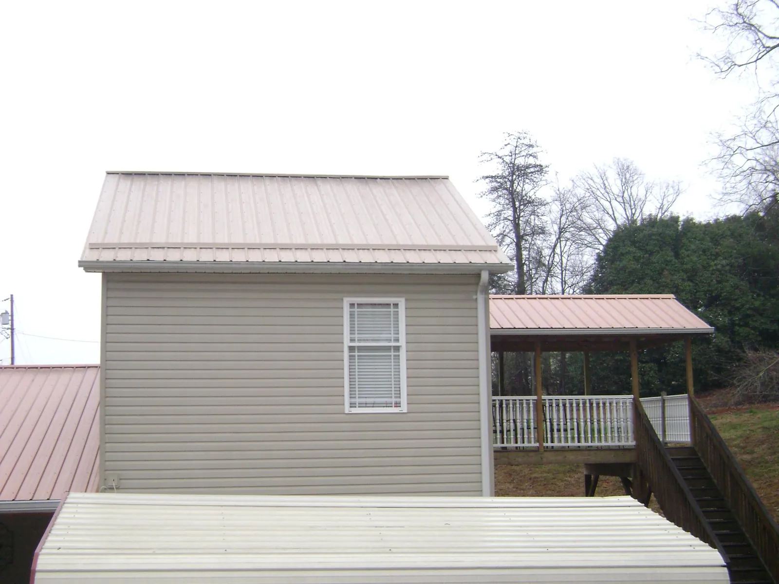 Tan metal roofs on a two story addition and attached porch, from a Roof Replacement job in Dell Rapids